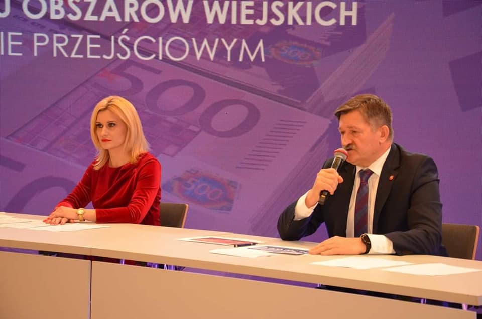 Zdjęcie przedstawiające dwie osoby, kobietę i mężczyznę siedzących przy stole konferencyjnym i udzielających wywiadu. Za nimi w tle znajduje się ogromny telebim z napisem Dodatkowe środki dla lubelskiego na działania Programu Rozwoju Obszarów wiejskich w okresie przejściowym Ponad 100 mln euro dla województwa lubelskiego na realizację Programu Rozwoju Obszarów Wiejskich na lata 2014-2020