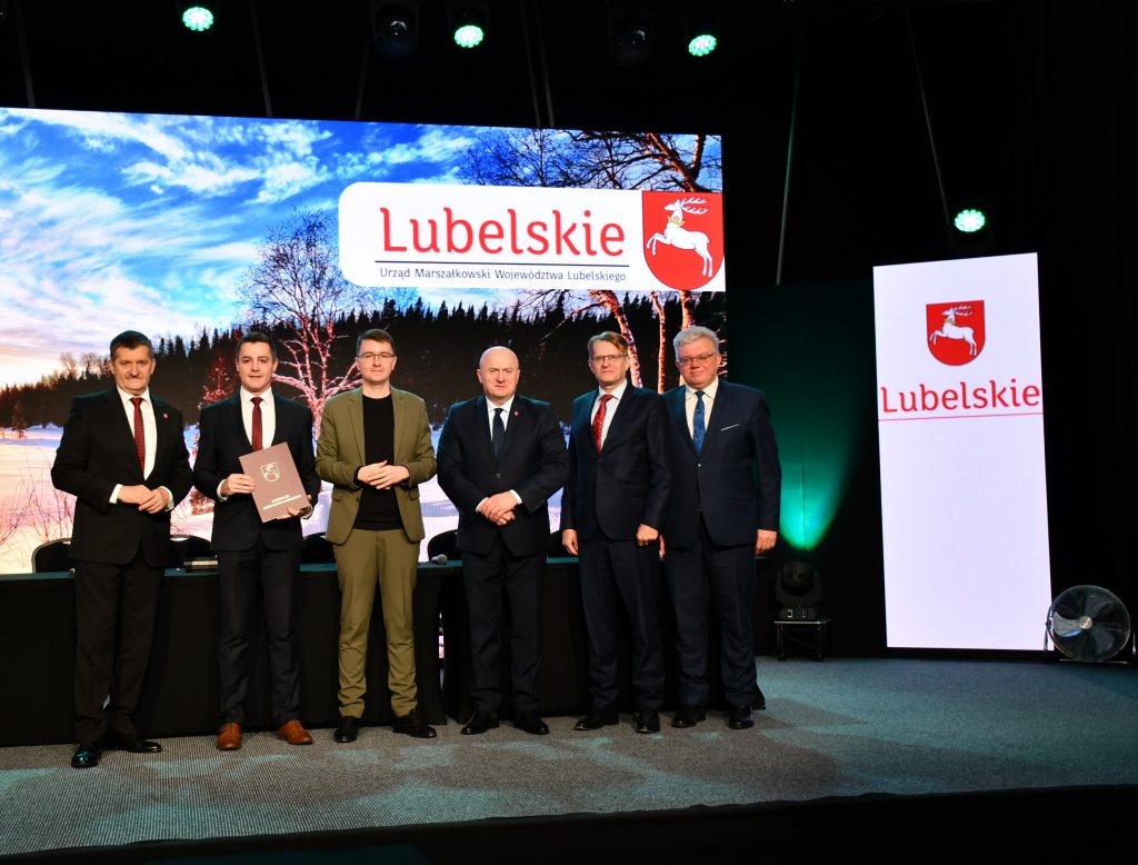 Zdjęcie przedstawia Członków Zarządu Województwa Lubelskiego wraz z przedstawicielem Lokalnej Grupy Działania podczas podpisania umowy. Pięciu mężczyzn w eleganckich garniturach, za nimi napis Lubelskie.