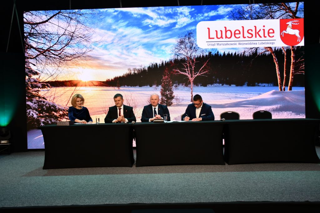 Zdjęcie przedstawia Członków Zarządu Województwa Lubelskiego wraz z przedstawicielem Lokalnej Grupy Działania podczas podpisania umowy. Trzech mężczyzn oraz jedna kobieta ubrani elegancko siedzący za stołem.
