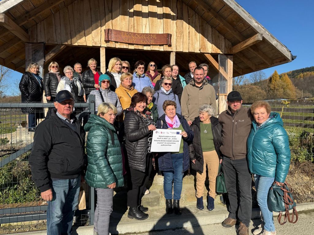 Grupa uczestników wyjazdu studyjnego do województwa podkarpackiego stoi na schodach przed drewnianą wiatą z szyldem Ekologiczne Kozie Sery.