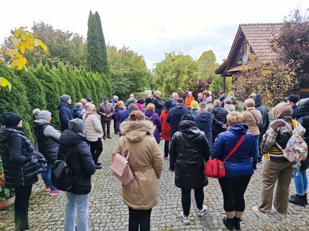 Uczestnicy wyjazdu studyjnego pod nazwą „Gospodarstwa ekologiczne” na Podlasie zwiedzają gospodarstwo państwa Romaniuków w Nowokornino. Jest to grupa licząca 50 osób. Stoją na podwórku, po prawej stronie jest dom, po lewej żywopłot. Gospodarz opowiada o pracy na swoim gospodarstwie.