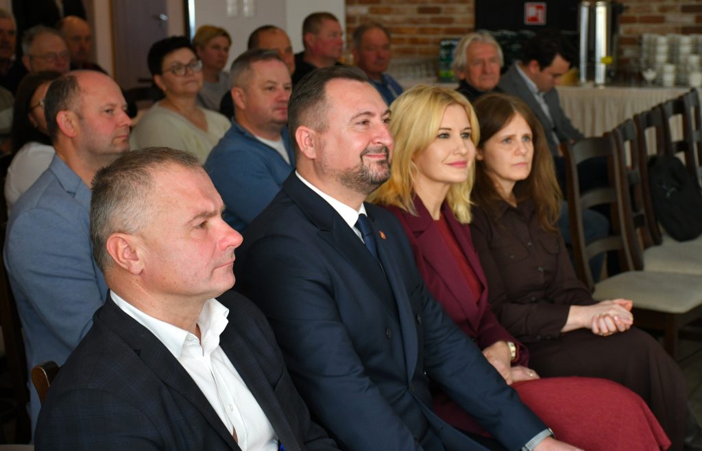 Grupa osób siedząca, na pierwszym planie dwie kobiety i dwóch mężczyzn ubranych elegancko.