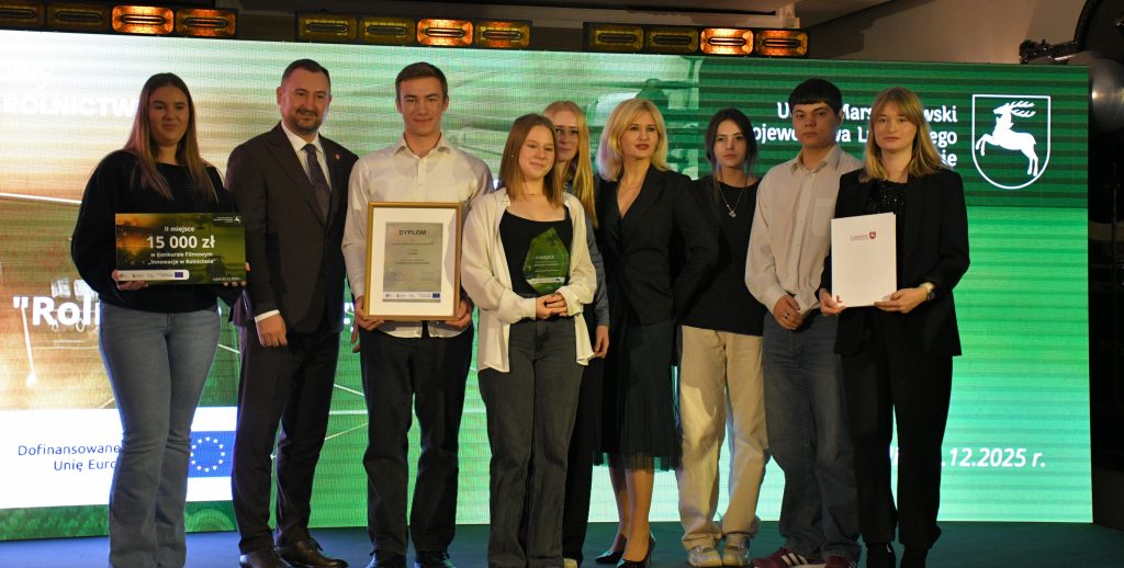 Na scenie, na tle kolorowej grafiki stoi grupa osób (pięć kobiet i trzech mężczyzn) ubranych elegancko, w dłoniach trzymają czek, statuetkę, dyplom i białą teczkę.