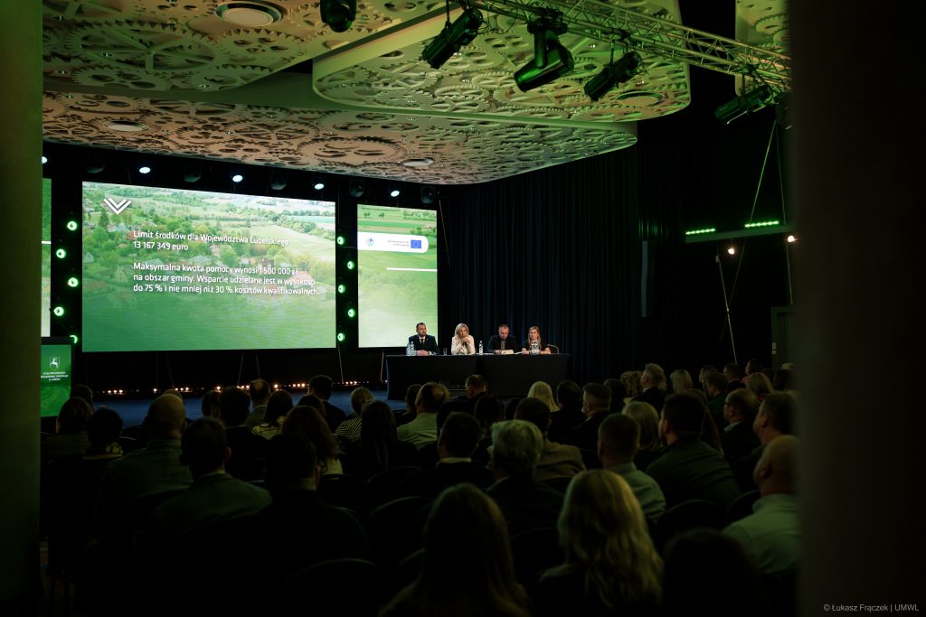 Zdjęcie przedstawia siedzącą publiczność. W tle scena z ekranem na którym napis: Limit środków dla Województwa Lubelskiego 13 167 349 euro. Z prawe strony ekranu eksperci siedzący za stołem.