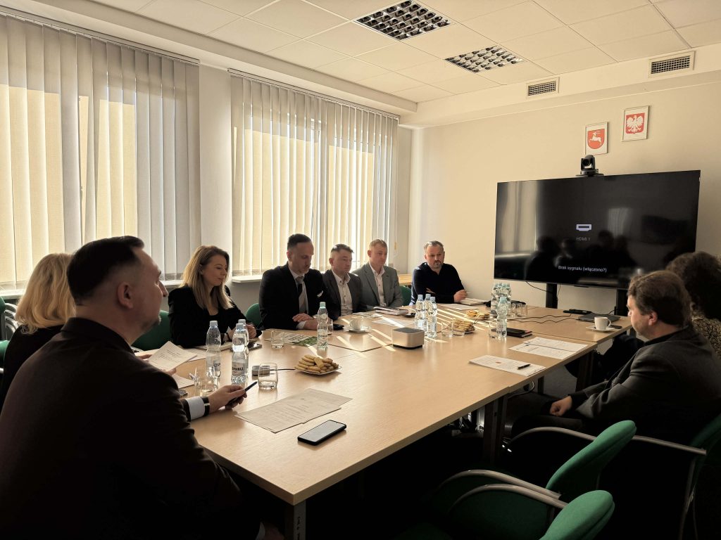 Członkowie Grupy Tematycznej do spraw chmielu elegancko ubrani siedzący przy stole. Przed stołem duży telewizor do połączenia zdalnego.