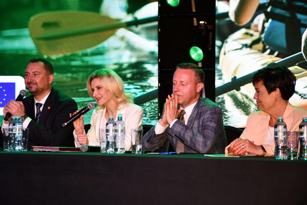 Za stołem prezydialnym podczas konferencji „Wsparcie rozwoju sportu, rekreacji i turystyki na obszarach wiejskich województwa lubelskiego w ramach Planu Strategicznego dla Wspólnej Polityki Rolnej na lata 2023–2027 – LEADER”, siedzą cztery osoby: od lewej strony wicemarszałek województwa lubelskiego Marek Wojciechowski, dyrektor Departamentu Rolnictwa i Rozwoju Obszarów Wiejskich Urzędu Marszałkowskiego Województwa Lubelskiego w Lublinie - Ewa Szałachwiej, radny województwa lubelskiego Michał Mulawa i zastępca dyrektora Departamentu Rolnictwa i Rozwoju Obszarów Wiejskich Urzędu Marszałkowskiego Województwa Lubelskiego w Lublinie – Dorota Kozak. Do uczestników konferencji przez mikrofon mówi dyrektor Ewa Szałachwiej.