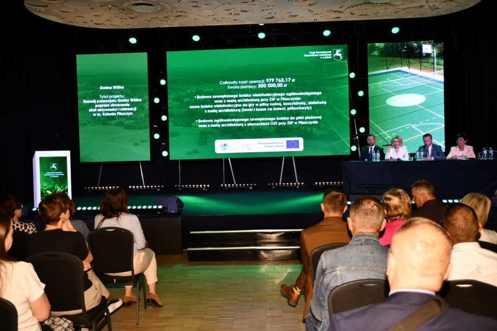 Uczestnicy konferencji „Wsparcie rozwoju sportu, rekreacji i turystyki na obszarach wiejskich województwa lubelskiego w ramach Planu Strategicznego dla Wspólnej Polityki Rolnej na lata 2023–2027 – LEADER” siedzą na Sali konferencyjnej i oglądają prezentację przedstawiającą dobre praktyki.